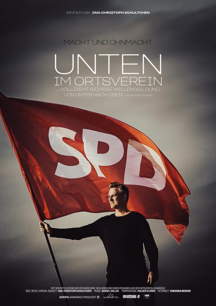 Filmplakat zu Unten Im Ortsverein, eine männliche Person mit entschlossenem Blick zur Seite hält eine rote SPD-Flagge vor einem stürmisch bedecktem Himmel.